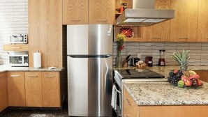 A modern kitchen with wooden cabinets, a stainless steel refrigerator, a microwave, and a granite countertop with fruits. - First Class Apartmet by Mr.W (Mexico City)