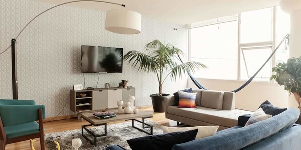A modern living room with a sofa, armchair, coffee table, and a TV on the wall.