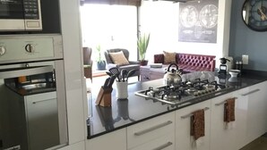 A modern kitchen with a central island, stainless steel appliances, and a view to a living area with a sofa and decorative items. - Polanco Pearl by Mr.W (Mexico City)