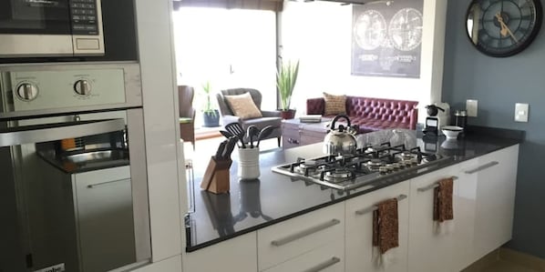 A modern kitchen with a central island, stainless steel appliances, and a view to a living area with a sofa and decorative items.