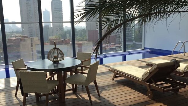 A balcony with a table and chairs, a lounge chair, and a view of the cityscape. - Polanco Pearl by Mr.W (Mexico City)