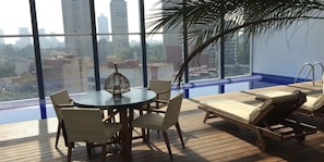 A balcony with a table and chairs, a lounge chair, and a view of the cityscape.