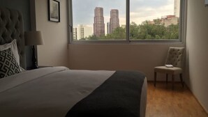 A bedroom with a large bed, a chair, a window with a city view, and a lamp. - Polanco Pearl by Mr.W (Mexico City)