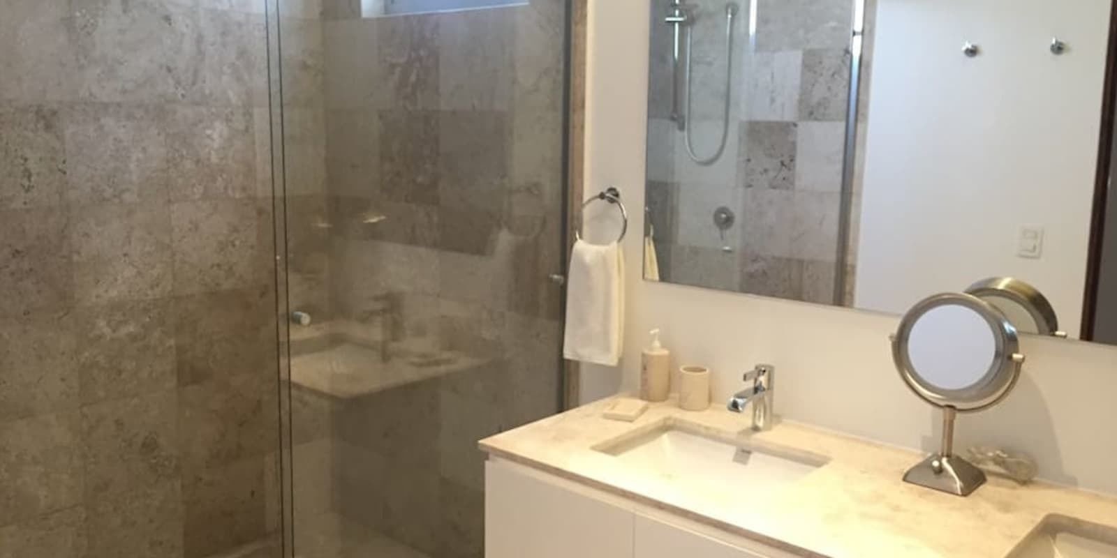 A modern bathroom with a glass shower enclosure, a vanity with a sink, a mirror, and toiletries.