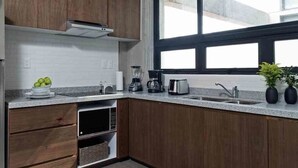 Moderni keittiö, jossa on puukaapit, ruostumattomasta teräksestä valmistettu jääkaappi, sisäänrakennettu mikroaaltouuni ja suuri ikkuna, josta tulee runsaasti luonnonvaloa.