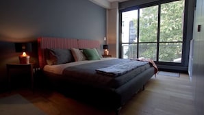 A modern bedroom with a large bed, two bedside tables with lamps, and a large window with a view of trees and buildings. - Unique Roma Town House by Mr.W (Mexico City)