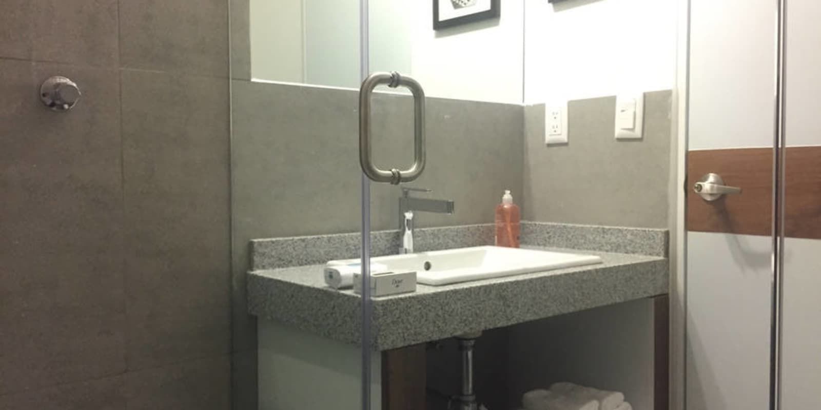 Une salle de bain avec un comptoir en granit, un lavabo blanc, un miroir et une cabine de douche en verre.