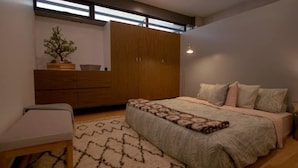 A bedroom with a bed, bedside table, lamp, wardrobe, and a small potted plant. - Unique Roma Town House by Mr.W (Mexico City)