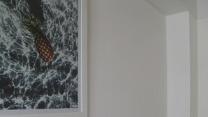 A room with a framed artwork depicting a pineapple amidst waves, a grey armchair, and a white wall. - Cactus Private Terrace by Mr.W (Mexico City)