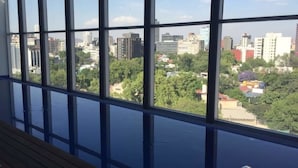 Ein Zimmer mit großen Fenstern und Blick auf eine Skyline mit Gebäuden und Grünflächen.