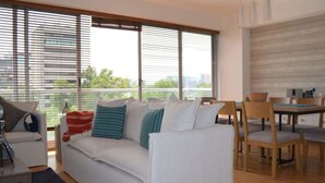 Ein modernes Wohnzimmer mit einem weißen Sofa, Kissen in Türkis und einem Essbereich mit Holzsesseln und einem Tisch.
