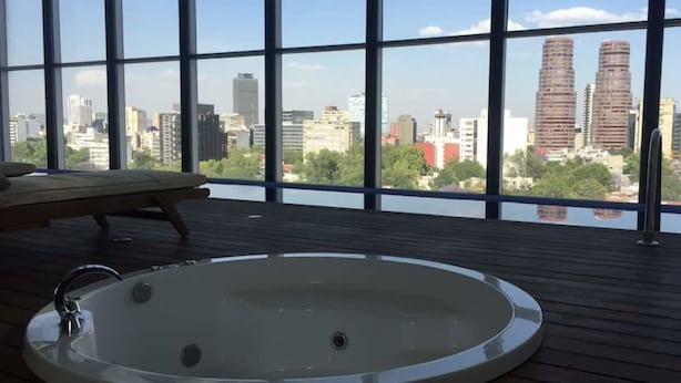 Ein Zimmer mit großem Fenster und Blick auf die Stadt, einer Holzdiele und einer runden Badewanne.