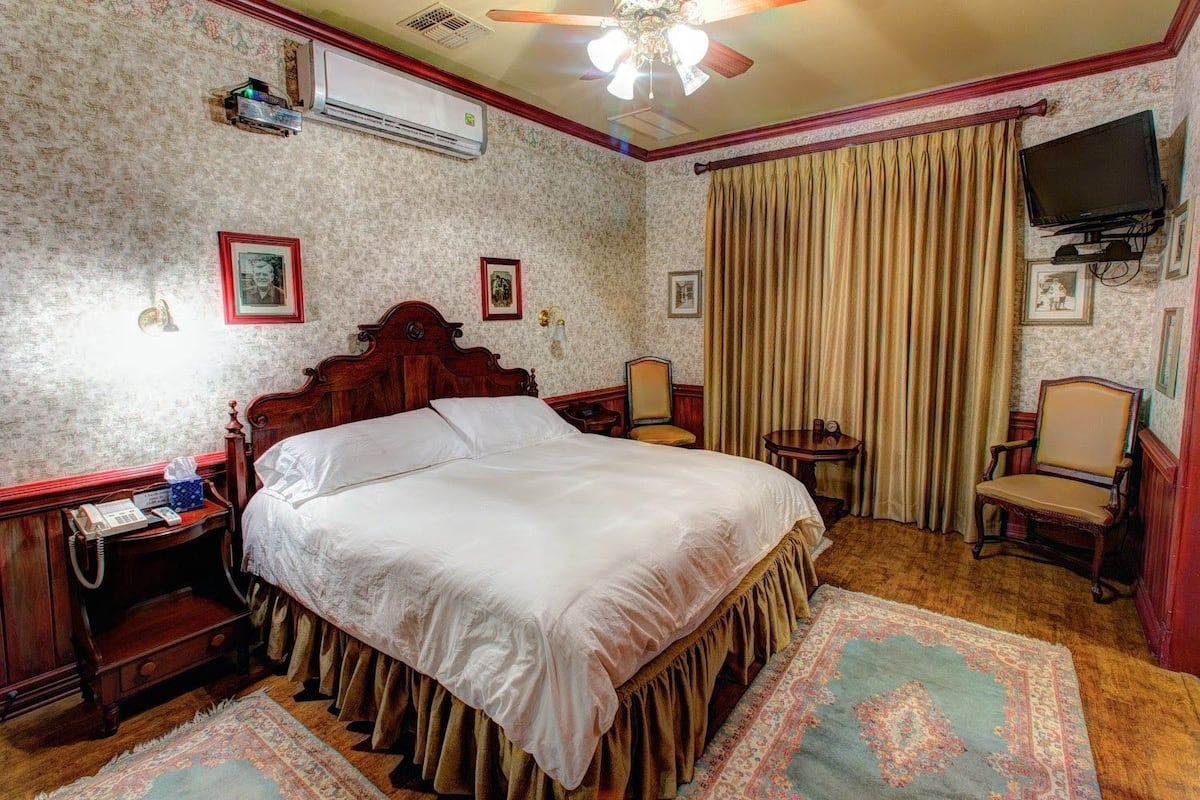 Une chambre à coucher de style traditionnel, avec un grand lit, une table de chevet en bois, un bureau, une chaise, un téléviseur et un ventilateur de plafond.