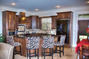 A kitchen with wooden cabinets, a central island with bar stools, a refrigerator, and a dining area with a red tablecloth.