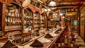 A bar with wooden shelves stocked with bottles and glasses, a long counter with tables and chairs, and a television mounted on the wall. - Kiepersol Bed and Breakfast (Tyler)