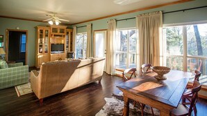 A spacious living room with a wooden dining table, a sofa, and a kitchen area with cabinets and a television. - Kiepersol Bed and Breakfast (Tyler)