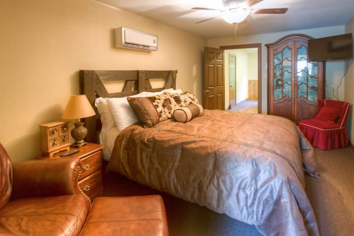 Une chambre à coucher avec un grand lit, une tête de lit en bois, une table de chevet avec une lampe, un fauteuil en cuir et une armoire.