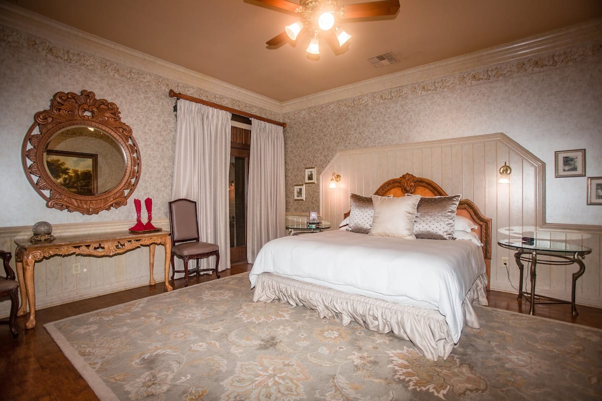 Une chambre à coucher avec un grand lit, une tête de lit en bois, un miroir rond, une petite table et une chaise.