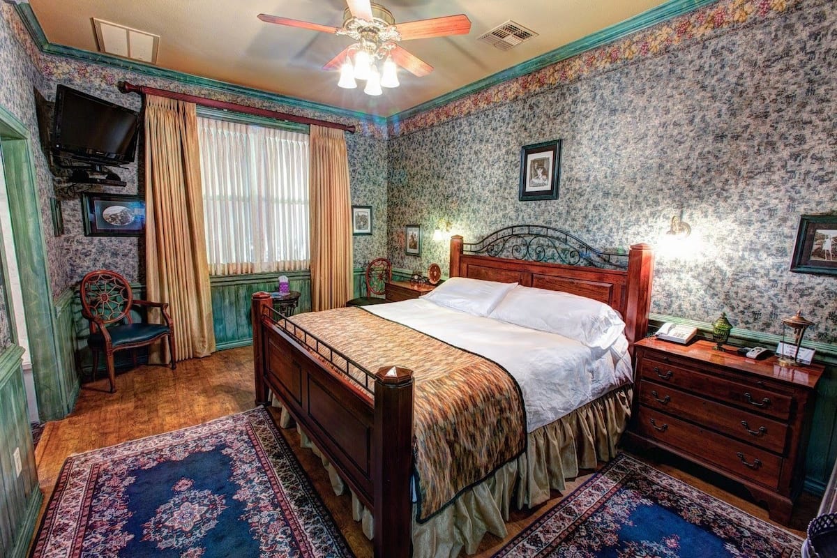 Une chambre à coucher de style traditionnel, avec un lit en bois, une table de chevet, une commode, une chaise, un téléviseur et une fenêtre avec des rideaux.