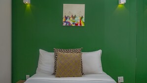 Un lit avec une literie blanche et des coussins à motifs, un mur vert et un tableau au-dessus du lit.