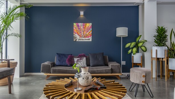 Un salon moderne avec un mur d’accent bleu foncé, une table basse ronde, un canapé avec des coussins et des plantes en pot.