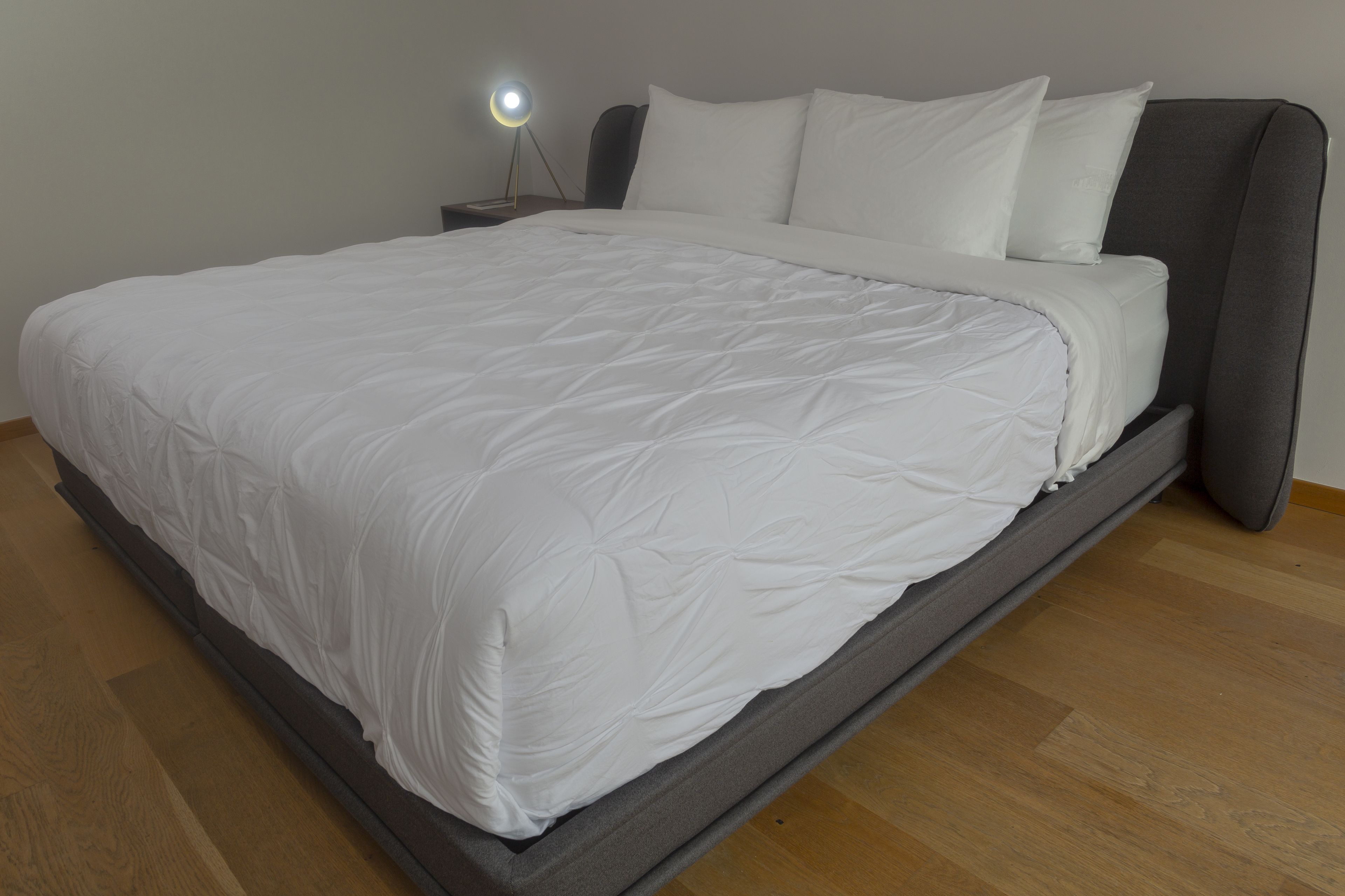 Un lit bien fait, avec du linge de lit blanc, une lampe de chevet et un plancher en bois.