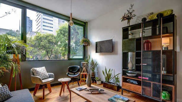 A modern living room with a large window, a sofa, a coffee table, a bookshelf, and various decorative items. - Zen Modern by Mr.W (Mexico City)