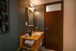 A bathroom with a wooden vanity, a mirror, and a sink. There is a shelf with towels and toiletries.