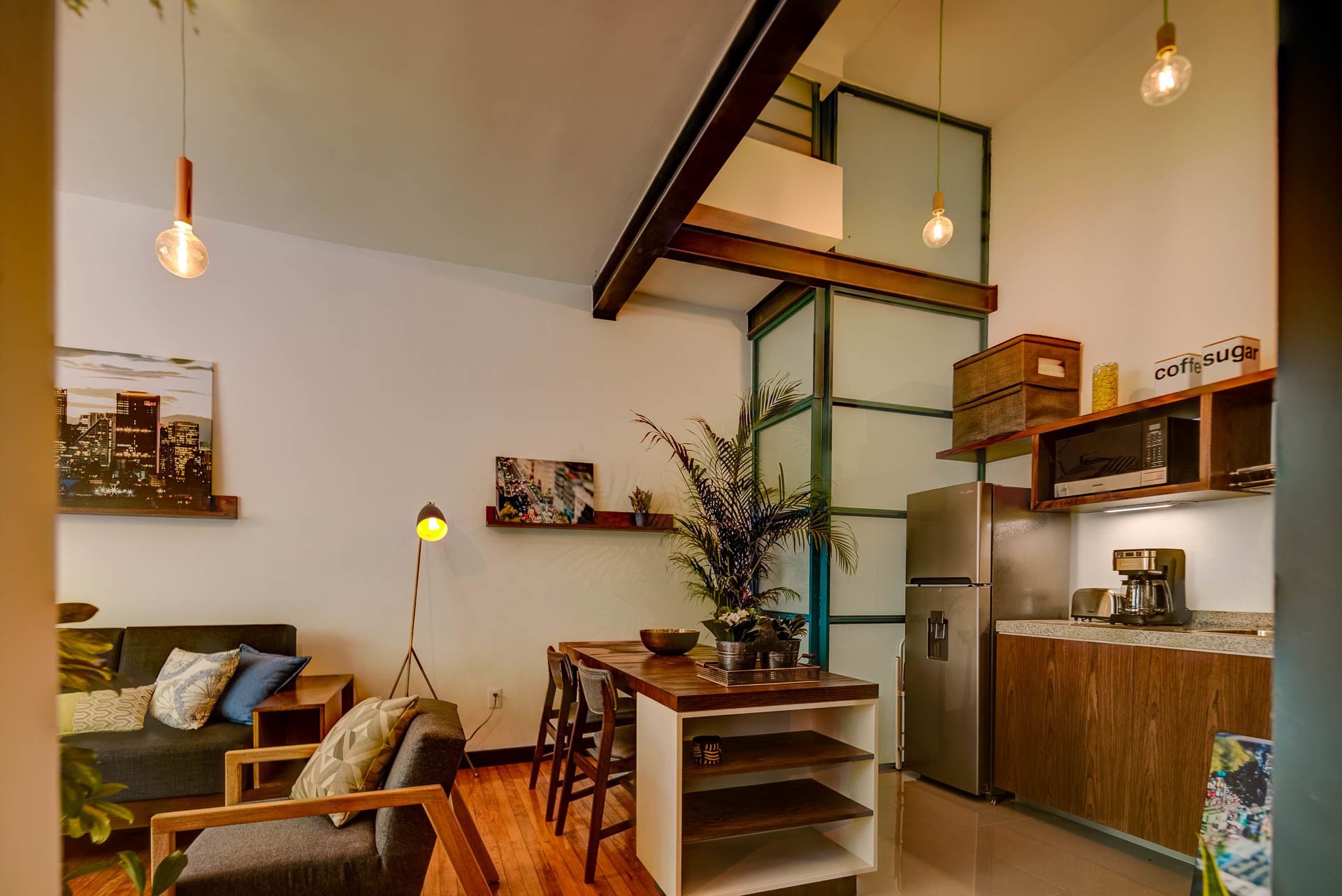 Une cuisine moderne équipée d’un réfrigérateur, d’un four à micro-ondes et d’une machine à café. On y trouve une table à manger avec des chaises, et une plante est posée sur la table.