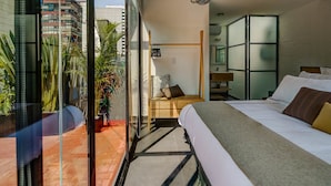 Habitación de hotel moderna con una cama grande, un escritorio pequeño, un espejo y vistas de la ciudad a través de amplios ventanales.