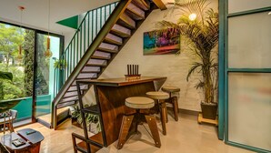 Un intérieur moderne avec un escalier en bois, un coin bar avec des tabourets et une grande plante en pot.