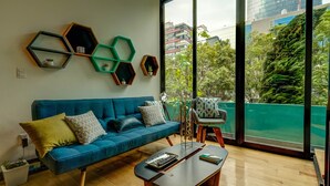 Un salon moderne avec un canapé bleu, une table basse en bois et une vue sur le paysage urbain, visible à travers de grandes fenêtres.