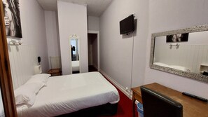 Une chambre d’hôtel avec un lit, une télévision, un miroir et une table en bois.