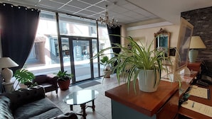 Een hotel lobby met een bank, een bijzettafeltje, een potplant, een spiegel, een lamp en een houten kast.