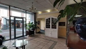 Een hotel lobby met glazen deur, een kroonluchter, een potplant, een kast met glazen deuren en een betegelde vloer.