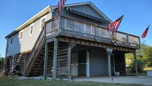 A two-story house with a wooden porch, two American flags, and a sign reading "Huggins 500". - OBX Beach Xanadu -  .7 miles to the beach plus HOTTUB! 🏖🏄‍♀️👙🩳🩱🩴🕶🏌‍♂️🚲  (Kill Devil Hills)