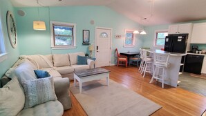 A cozy living room with a sofa, coffee table, and dining area. There is a kitchen with a refrigerator and a sink. - OBX Beach Xanadu -  .7 miles to the beach plus HOTTUB! 🏖🏄‍♀️👙🩳🩱🩴🕶🏌‍♂️🚲  (Kill Devil Hills)