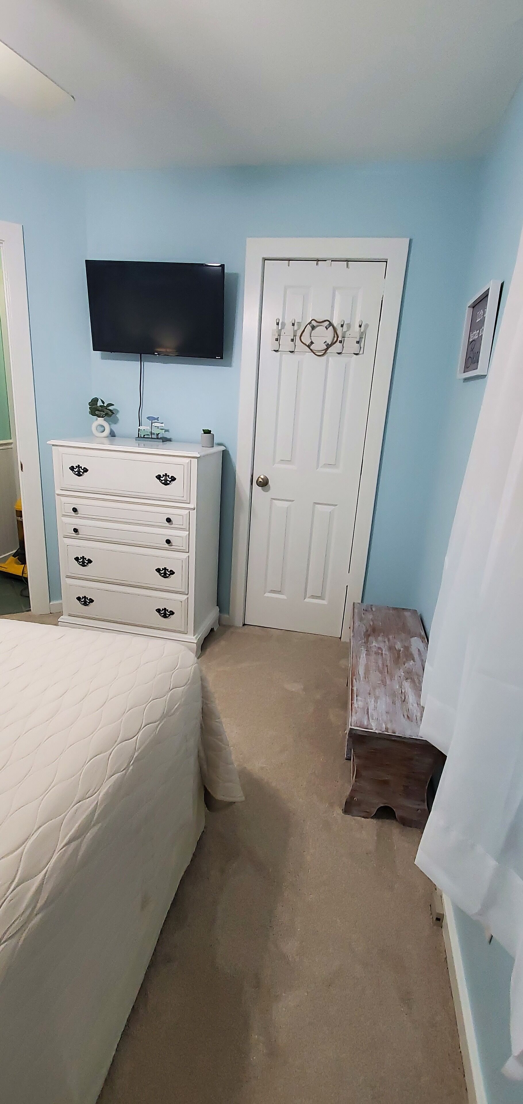 A bedroom with a bed, a dresser, a television mounted on the wall, and a door with a decorative handle.