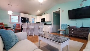 A compact living space with a kitchen, dining area, and a TV mounted on the wall. - OBX Beach Xanadu -  .7 miles to the beach plus HOTTUB! 🏖🏄‍♀️👙🩳🩱🩴🕶🏌‍♂️🚲  (Kill Devil Hills)