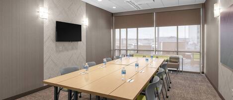 A conference room with a long table, chairs, a flat-screen TV, and a large window with a view.