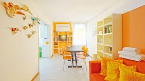 A bright living room with a dining area, orange furniture, and a bookshelf. - DolceVita Apartments N. 146 (Venice)