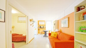 A bright, well-lit room with a sofa, a small table, and a bed. There is a bookshelf with books and decorative items. - DolceVita Apartments N. 146 (Venice)