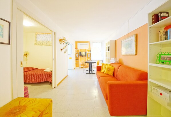 A bright, well-lit room with a sofa, a small table, and a bed. There is a bookshelf with books and decorative items. - DolceVita Apartments N. 146 (Venice)