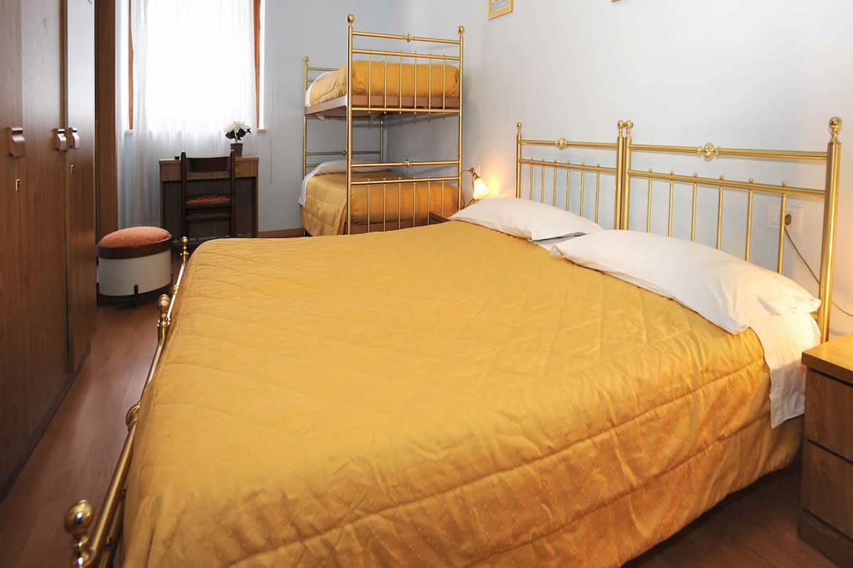 A bedroom with a large bed, a wooden wardrobe, a desk, and a chair.