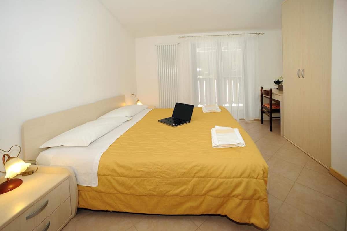 A hotel room with a bed, a laptop, a desk, and a chair.