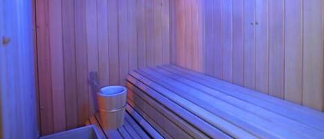 A sauna with wooden walls and benches, a skylight, and a trash bin.