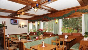 A cozy restaurant with wooden furniture, green cushioned benches, and large windows with flower arrangements. - Hotel Bucaneve (Moena)