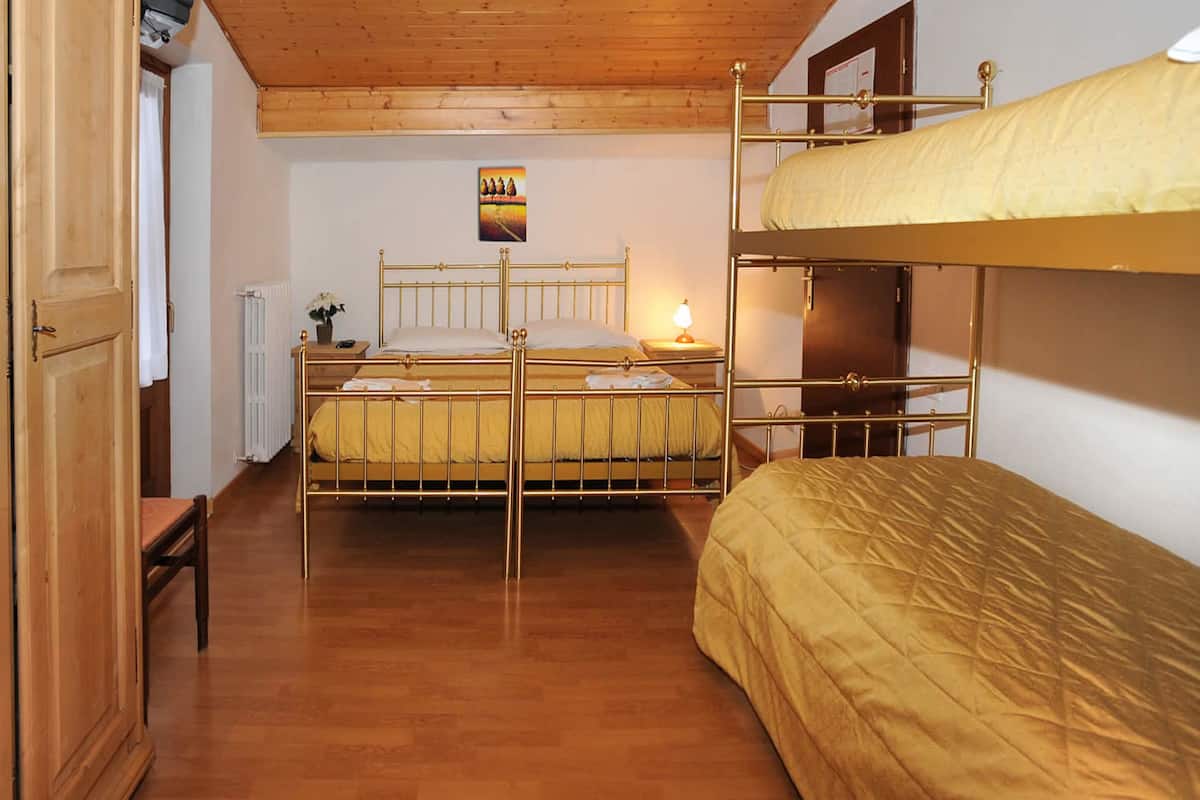 A room with a bunk bed, a wooden wardrobe, a bedside table with a lamp, and a radiator.