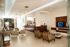 A modern hotel lobby with a reception desk, seating area, and a television.