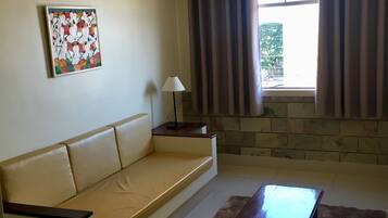 Una sala de estar con un sofá color crema, una mesa de centro de madera, una lámpara, un cuadro en la pared y un ventanal con cortinas.